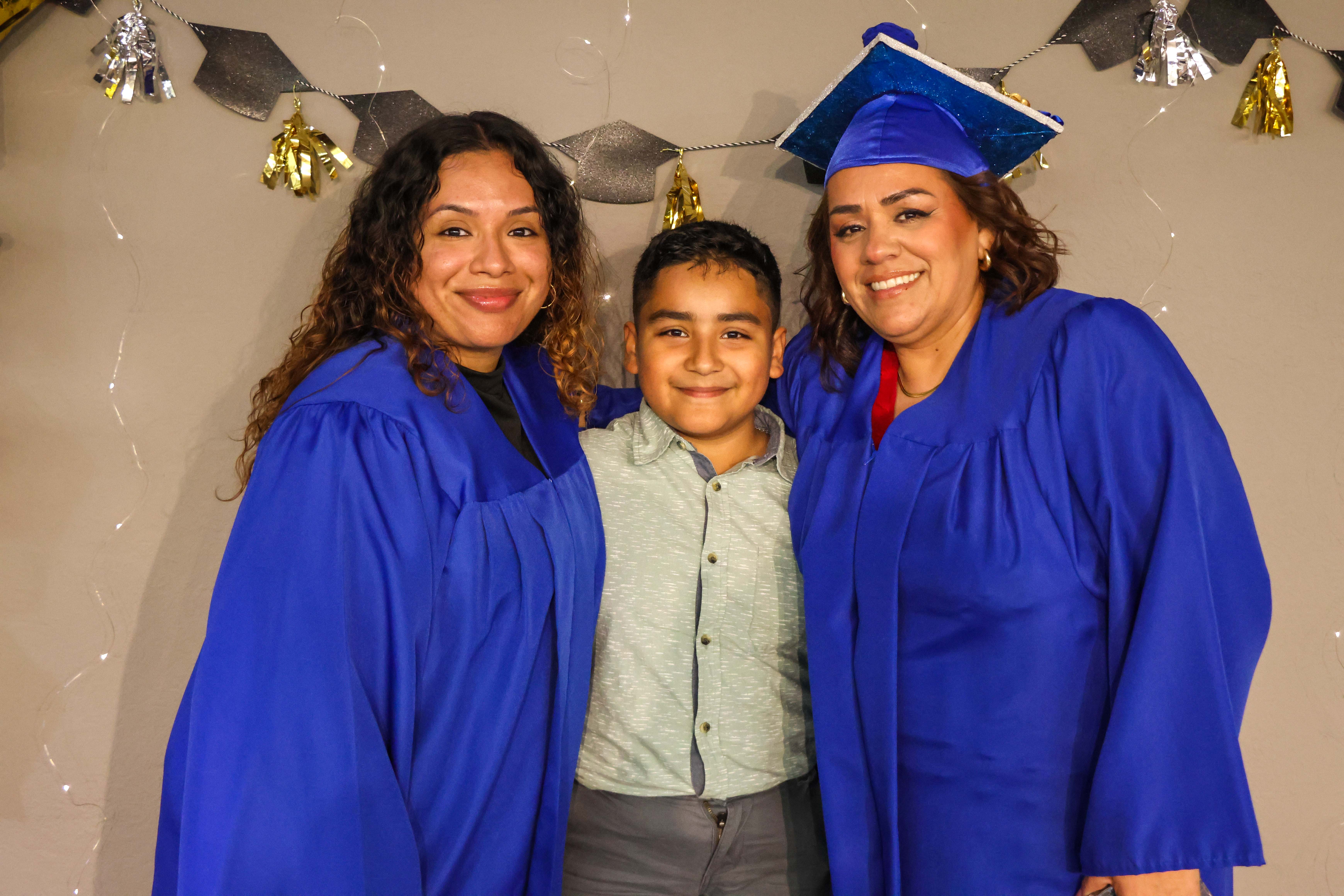 Two adult learners with a child posing in graduation cap and gown.
